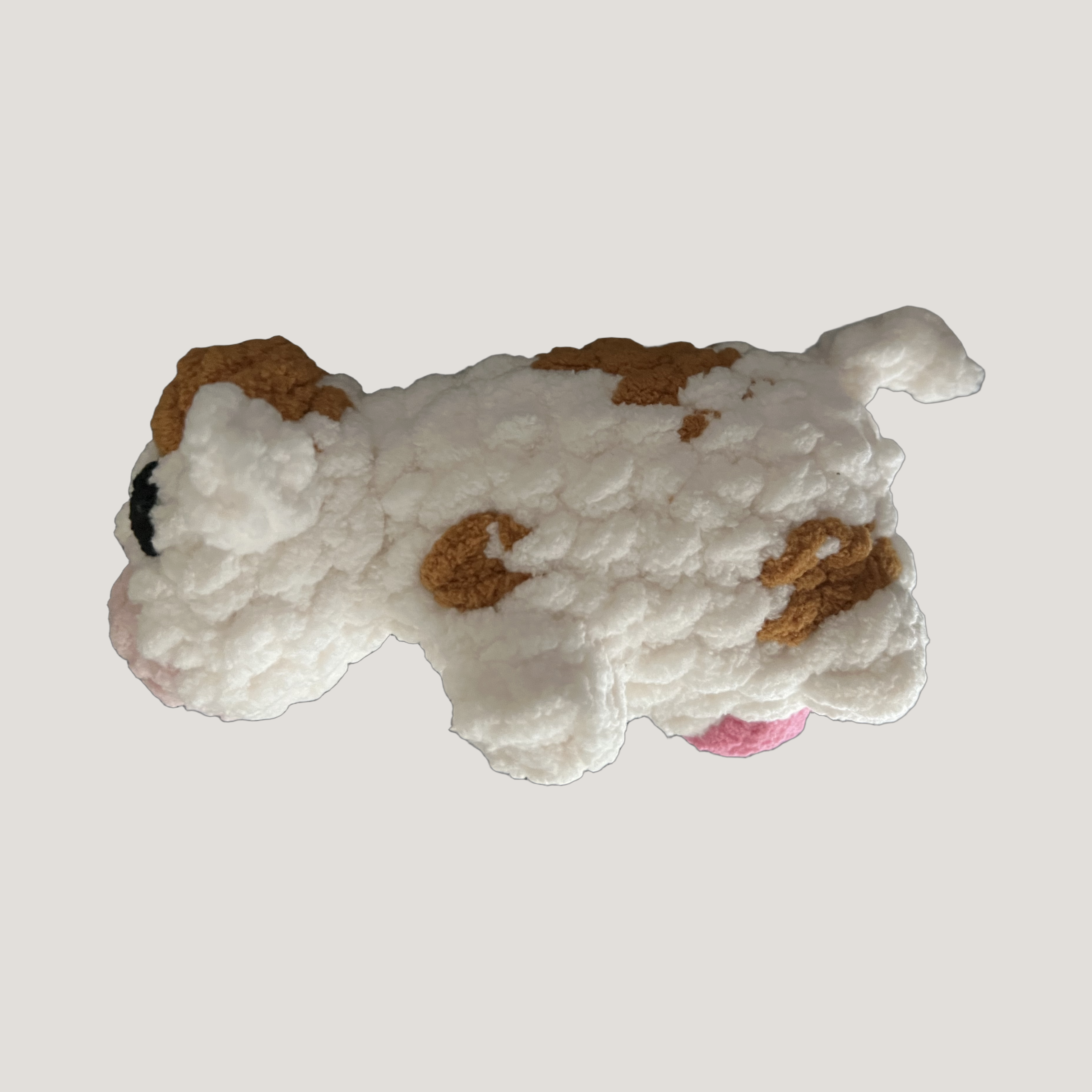 A small plush cow toy with a chunky, textured white fur-like body, brown patches, a pink nose, and a black nose, shown against a solid light gray background.